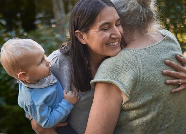 Overwhelmed woman holding a baby hugs her demanding mother-in-law
