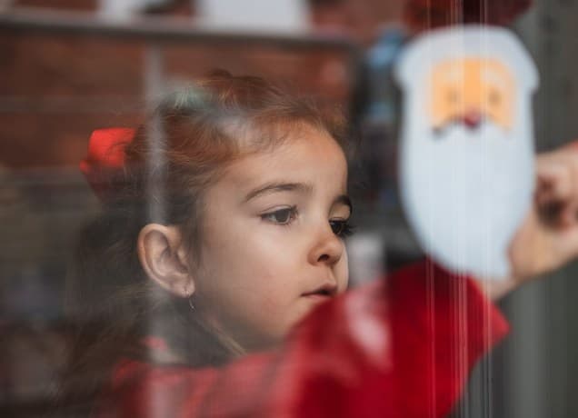 Little girl looks through Christmas decorated window