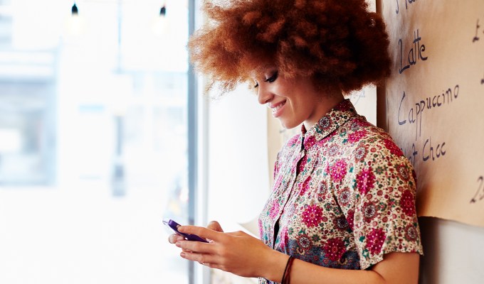 what to text after being ghosted: woman with an afro wearing a floral button up looks at her phone